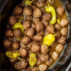 A slow cooked filled wtih cooked meatballs, a thin sauce, and several pepperoncini peppers.