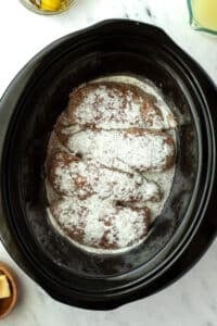 Sprinkling ranch seasoning on top of chicken breasts in a slow cooker.