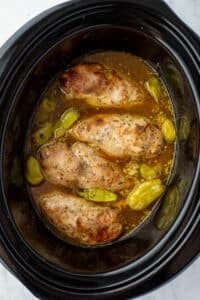 Chicken cooked in a slow cooker with seasoning, broth, and pepperoncini peppers.