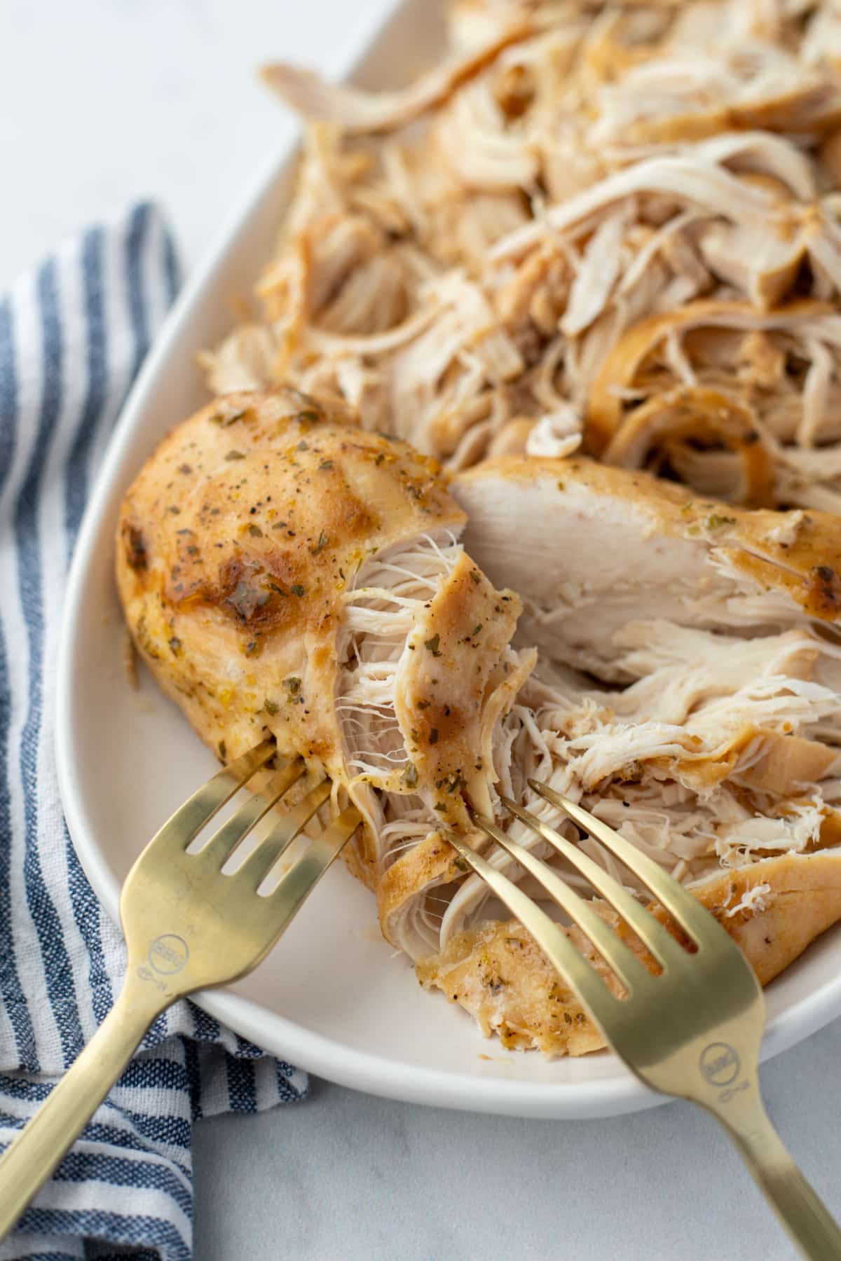 Shredding cooked chicken on a plate with two forks.