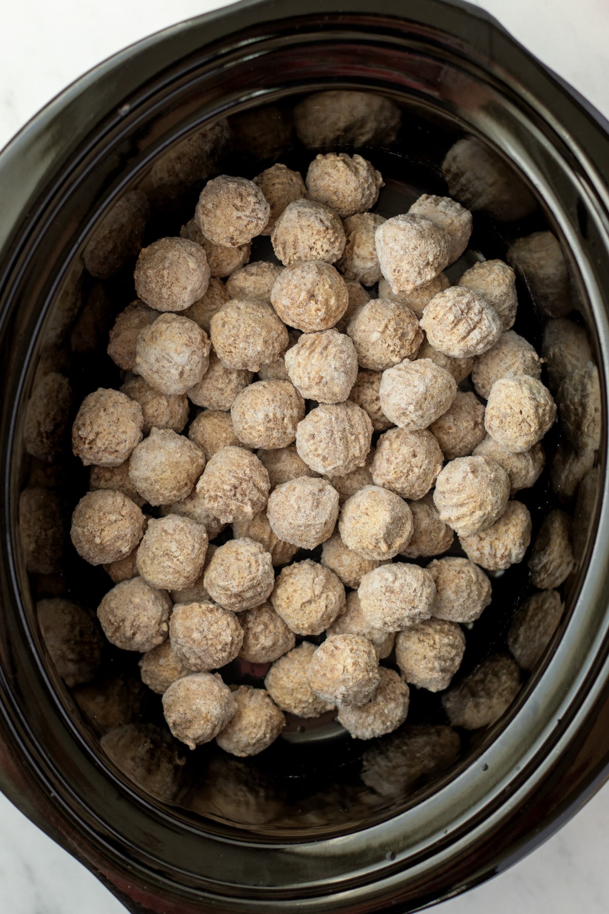 A slow cooker filled with frozen meatballs.
