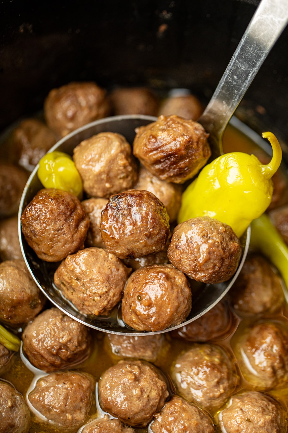 A ladle full of meatballs with pepperoncini peppers.