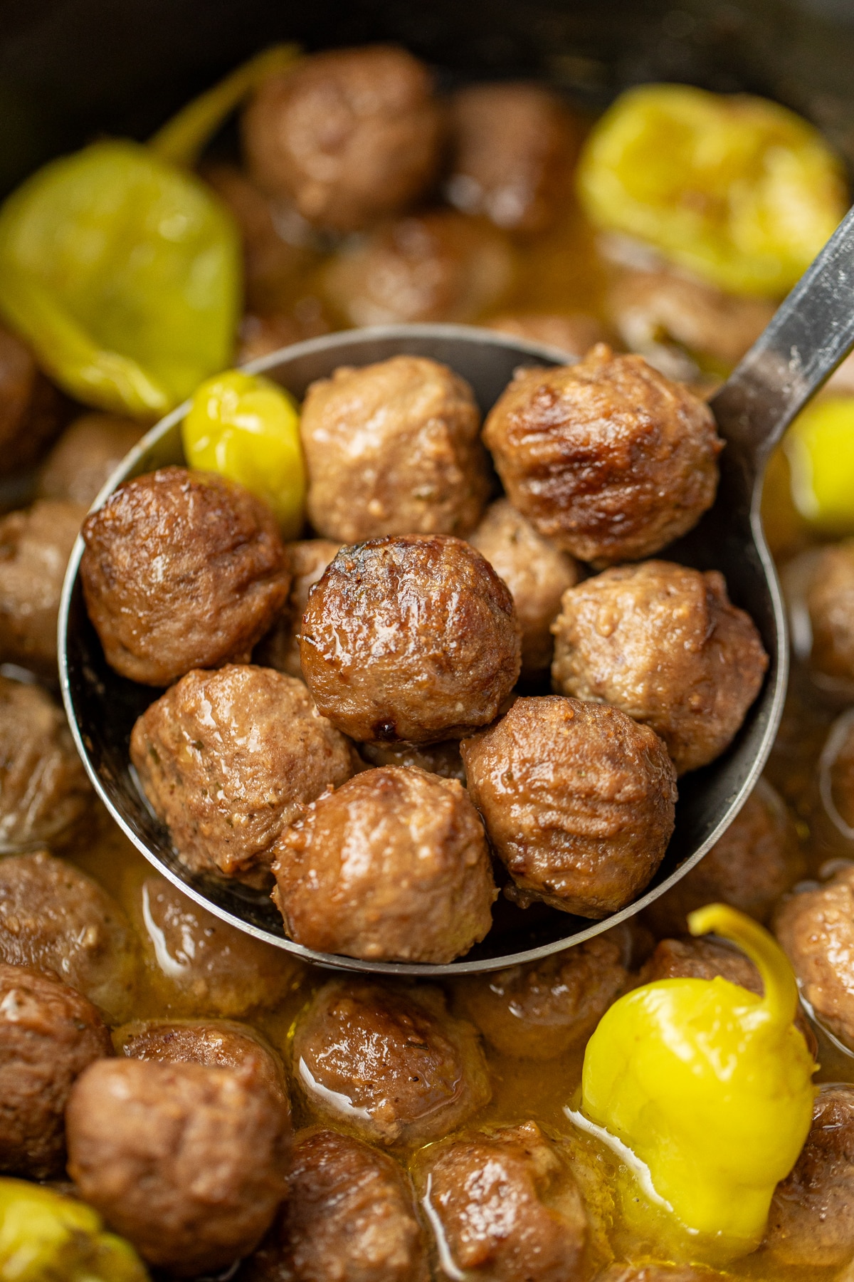 Scooping a ladle full of cooked meatballs from a large crock.