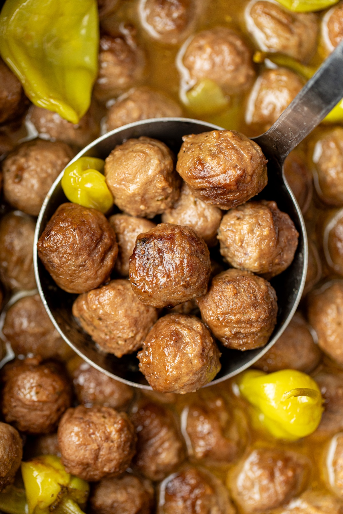 A ladle full of meatballs, with several scattered pepperoncini peppers around.