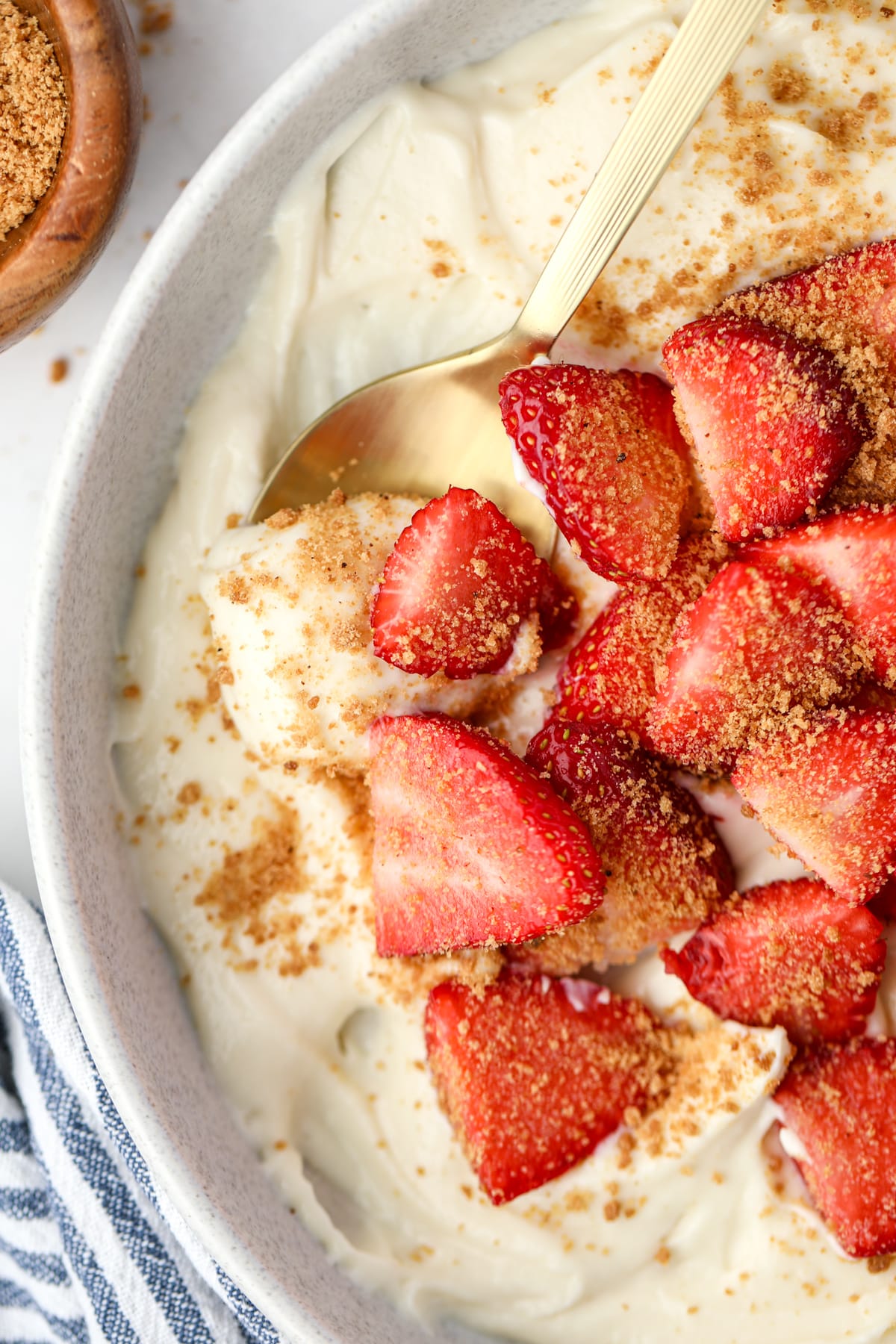 A spoon taking a portion of yogurt from a bowl topped with strawberries.