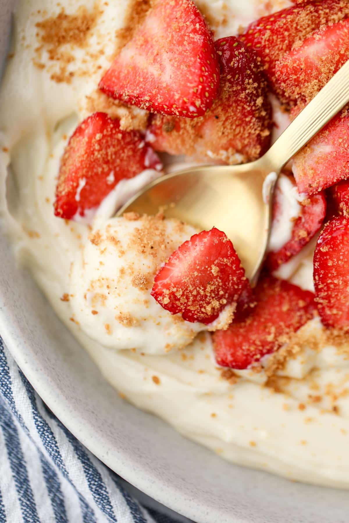 A close up of a spoon scooping yogurt from a bowl with fresh strawberries.