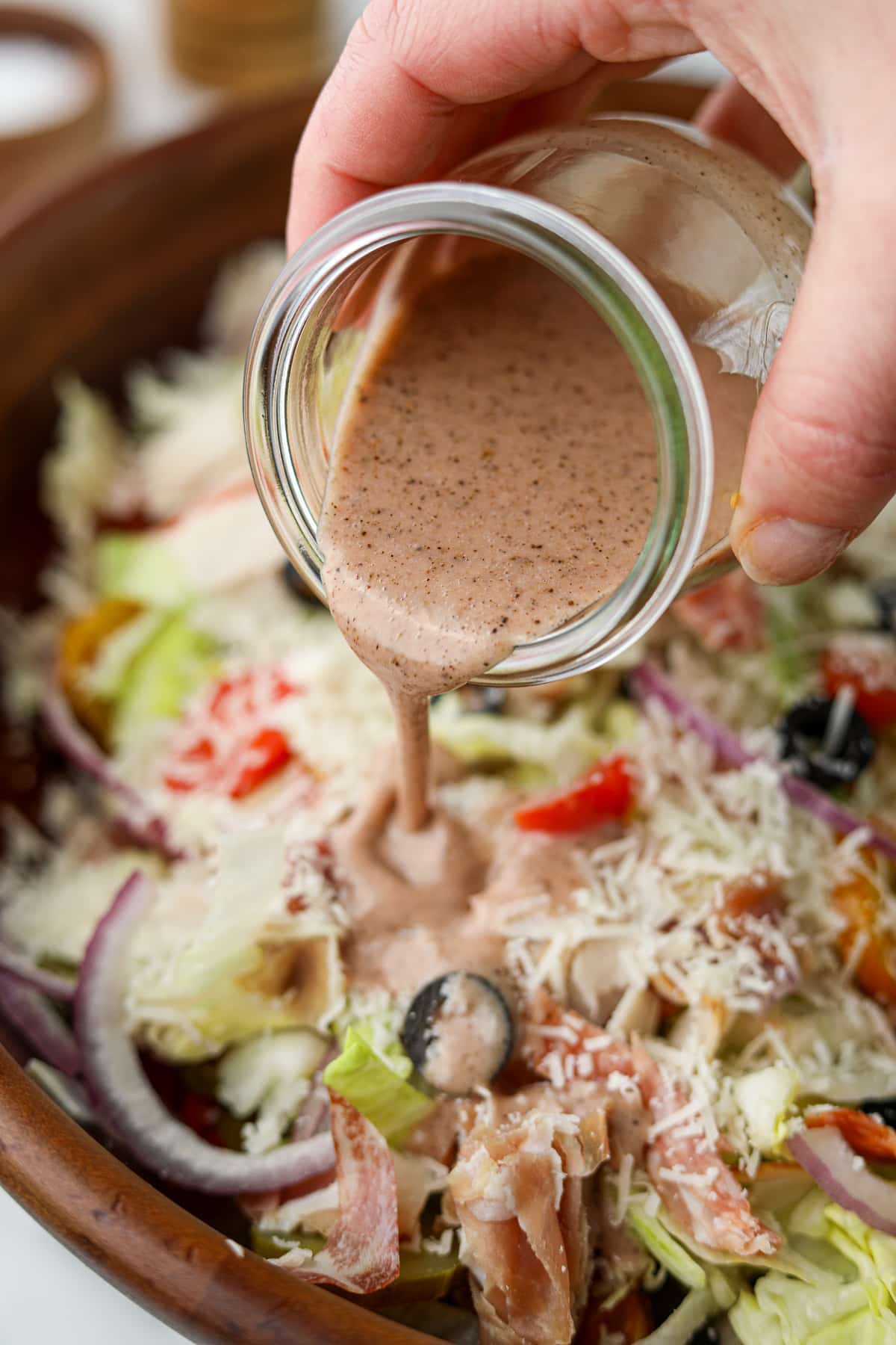 Drizzling sub sauce on top of a chopped salad with red onion, tomato, and lettuce.