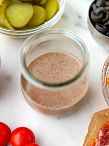 A small jar of sub sauce, surrounded by sub fillings.