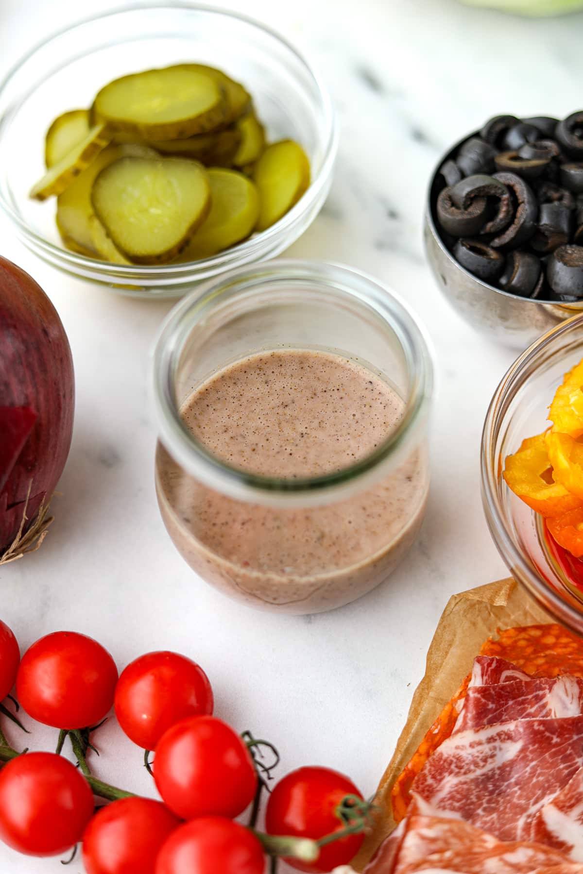 A small jar of sub sauce, surrounded by sub fillings.
