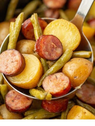 Scooping cooked potatoes, green beans, and smoked sausage from a slow cooker.