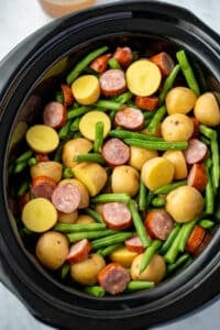 A slow cooker filled with potatoes, green beans, and smoked sausage.