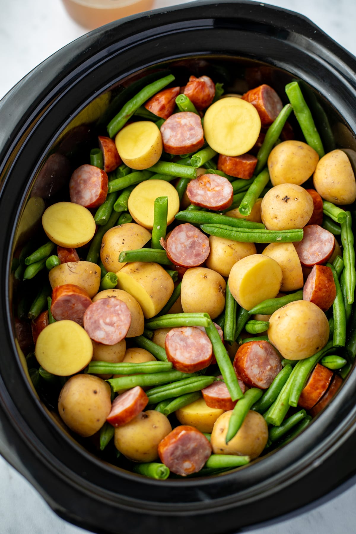 A slow cooker filled with potatoes, green beans, and smoked sausage.