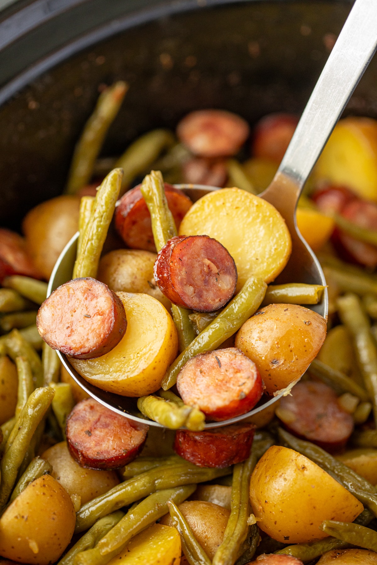 Scooping potatoes, green beans, and sausages out of a slow cooker.