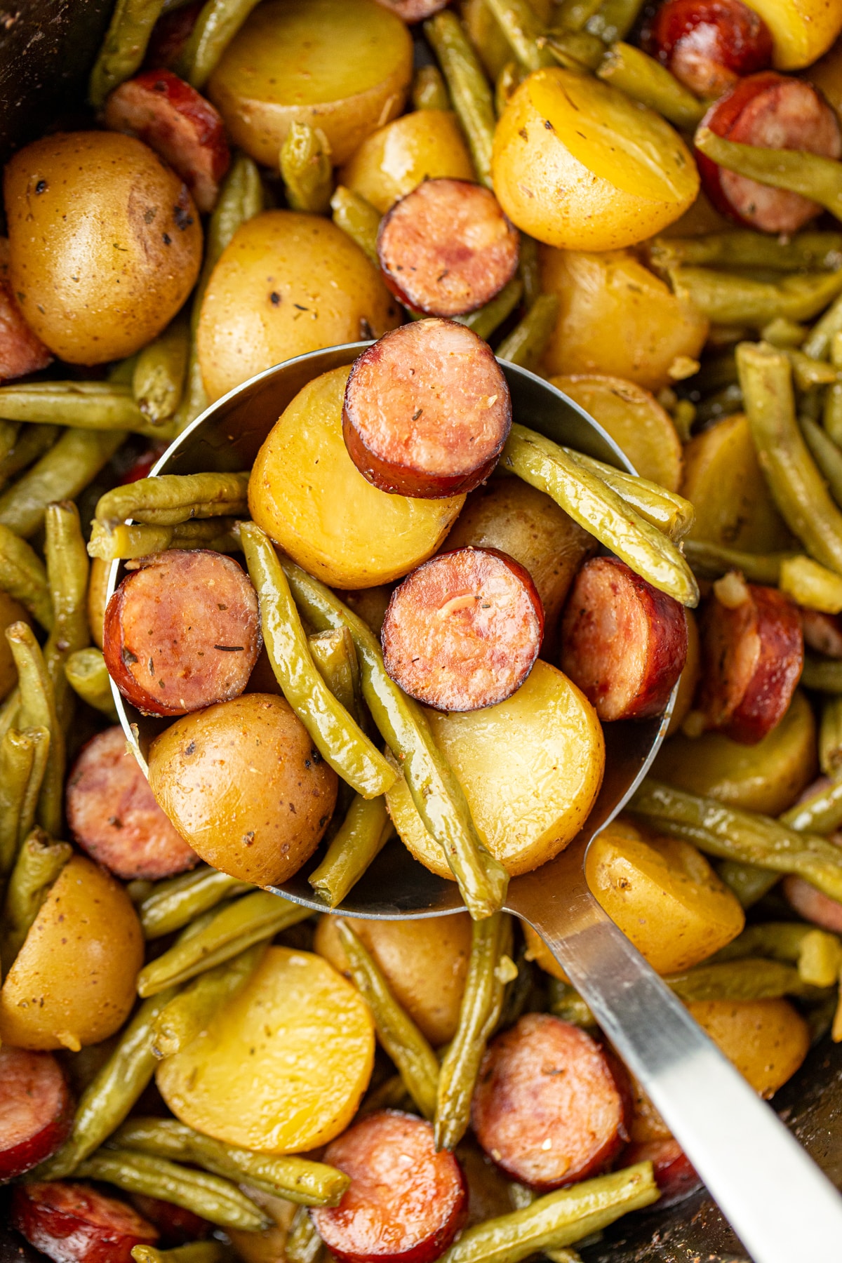 Scooping potatoes and sausage from a slow cooker.