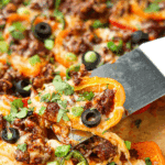 Carefully removing a bell pepper topped with melted cheese from a sheet pan.