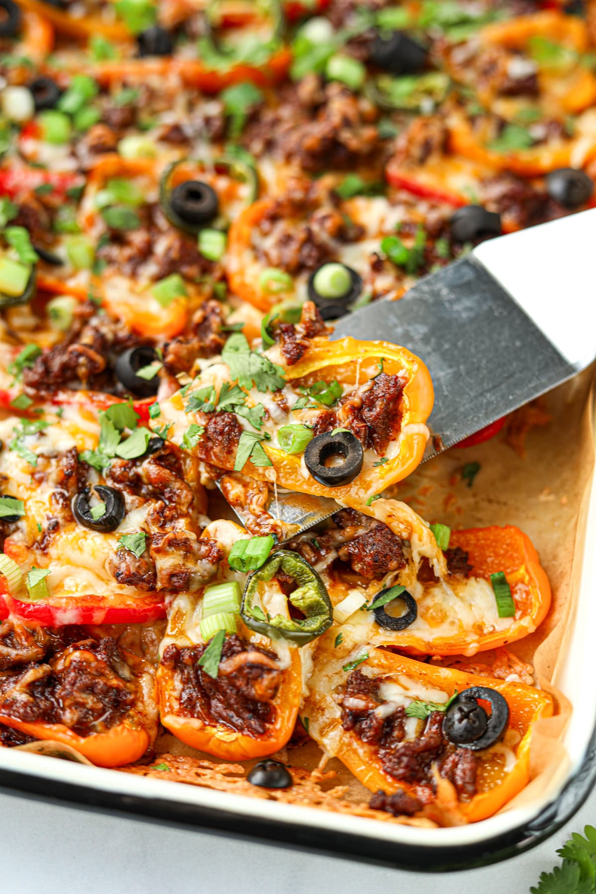 Carefully lifting bell pepper nachos from a sheet pan with a small spatula.
