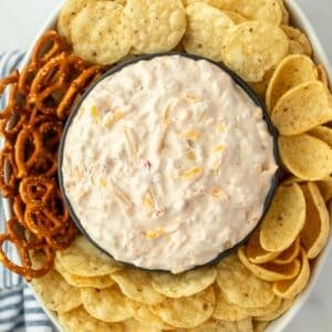 An oval dish filled with tortilla chips and other dippables, with a bowl of creamy cheese and corn dip in the center.