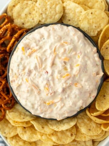 An oval dish filled with tortilla chips and other dippables, with a bowl of creamy cheese and corn dip in the center.