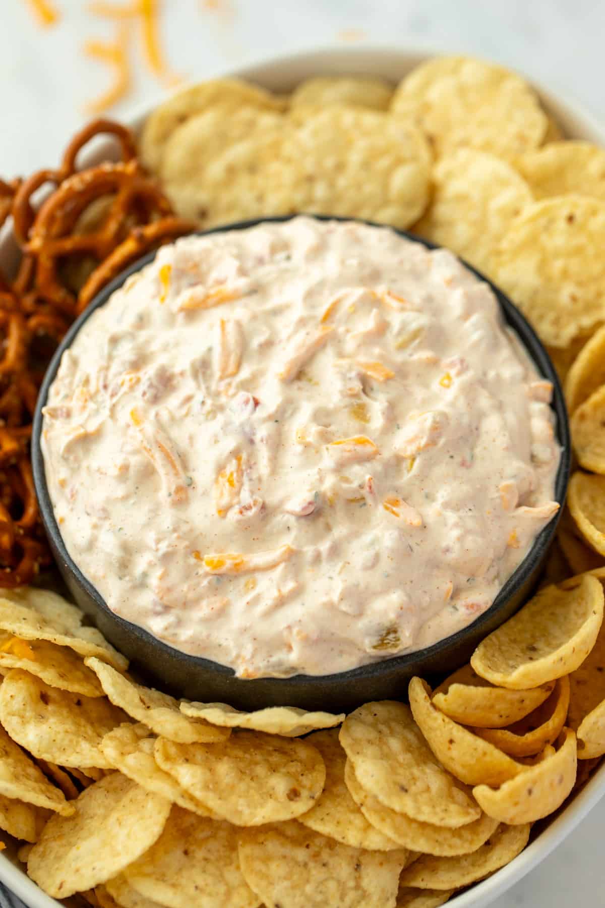A bowl of creamy dip surrounded by tortilla chips, corn chips, pretzels, etc.