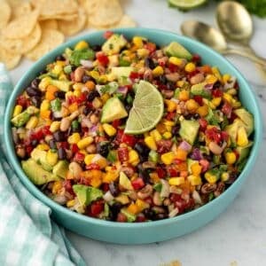 A bowl of cowboy caviar with tortilla chips in the background; topped with a lime wedge.
