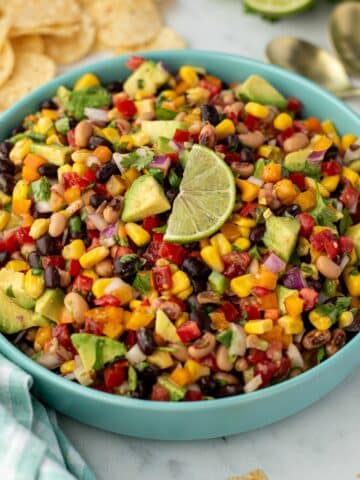 A bowl of cowboy caviar with tortilla chips in the background; topped with a lime wedge.
