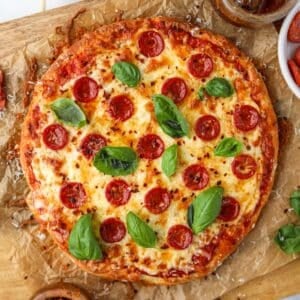 A pizza on parchment paper, topped with pepperoni, cheese, and fresh basil.