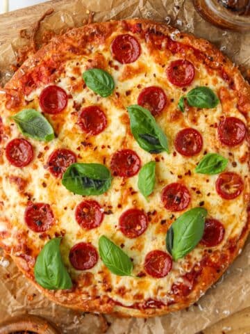A pizza on parchment paper, topped with pepperoni, cheese, and fresh basil.