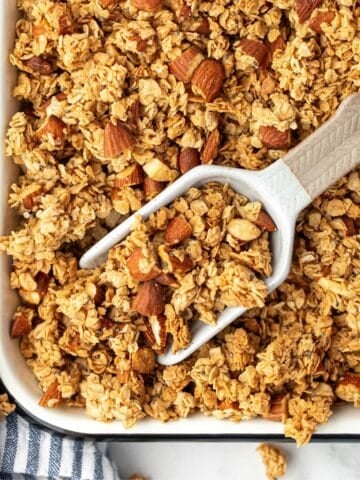A scoop taking a portion of granola from a baking pan.