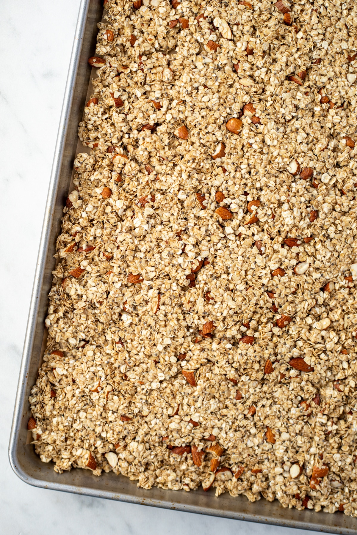 A sheet pan filled with granola ready to be baked, dotted with chopped almonds.
