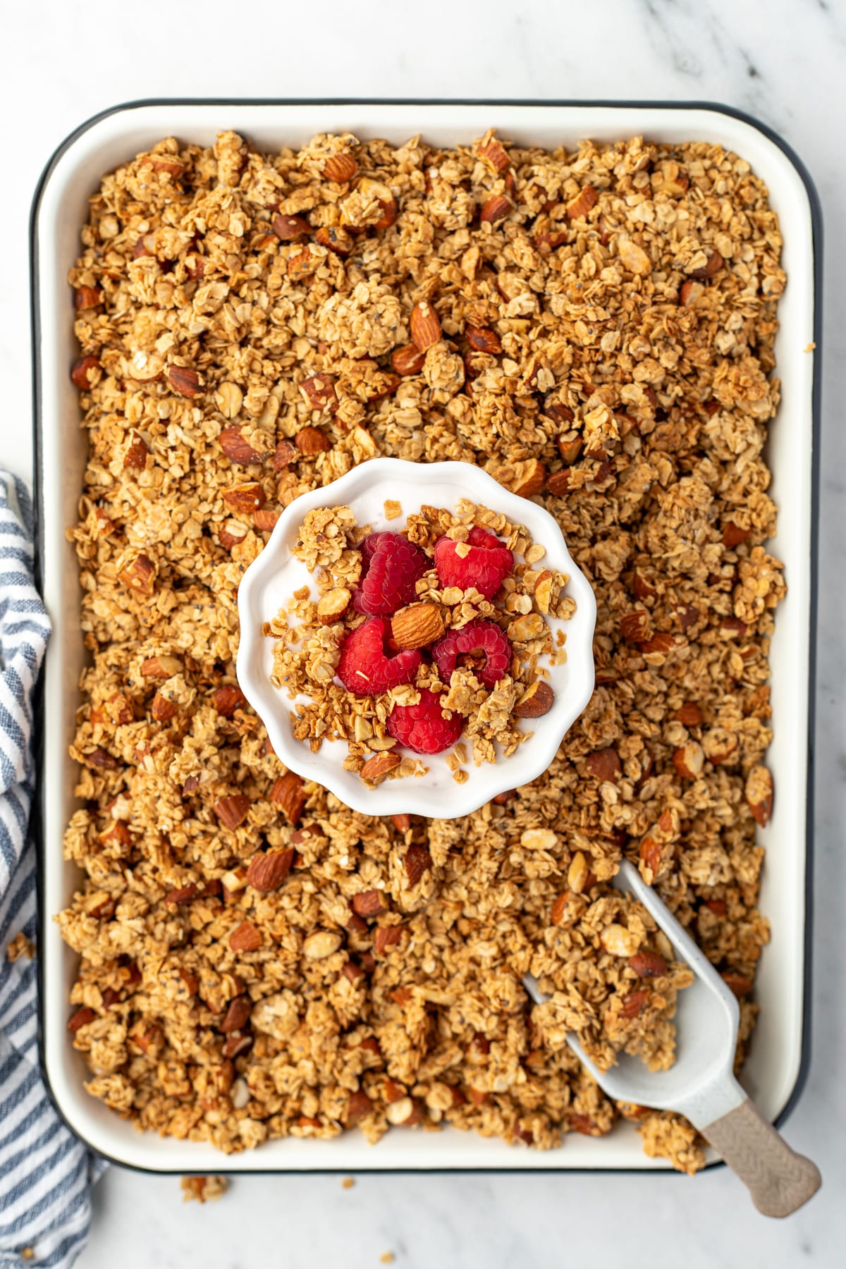 A sheet pan filled with granola, with a small bowl of yogurt and berries in the middle.