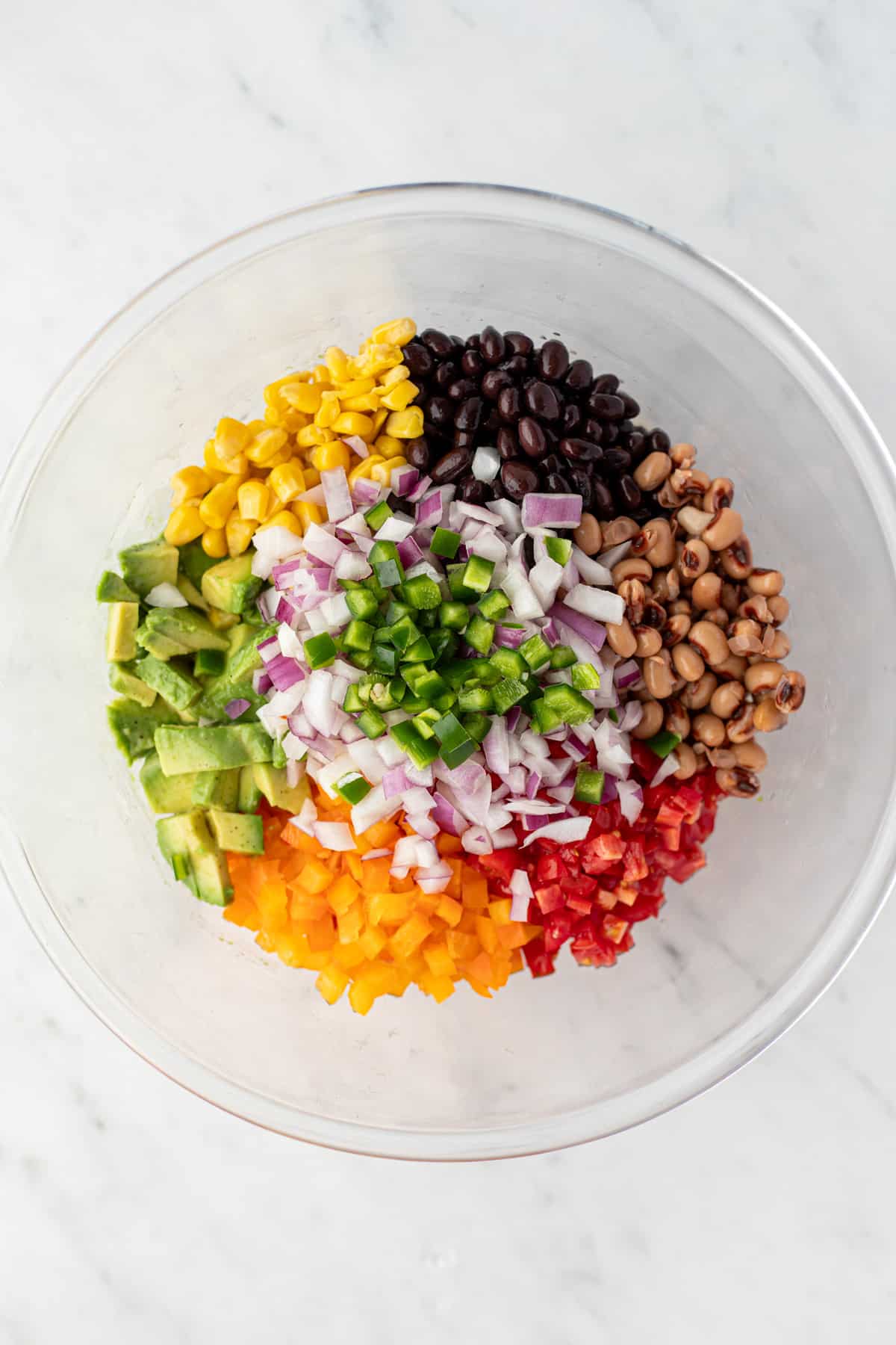 A bowl filled with a variety of fresh ingredients such as corn, bell pepper, tomato, red onion, etc.