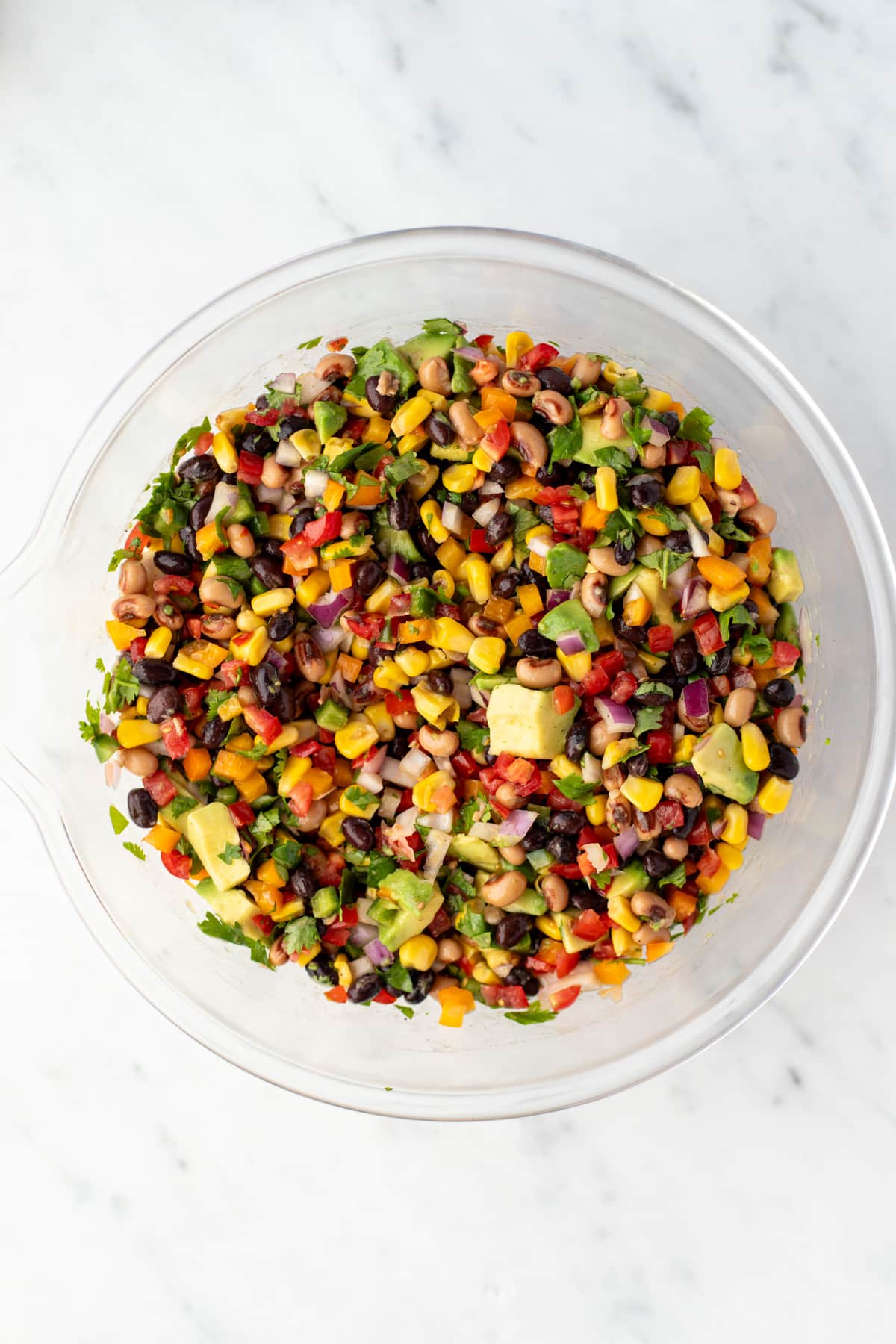 A bowl of bean salad with avocado and corn.