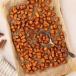 A sheet pan filled with roasted sweet potato cubes, with a spoon taking a portion.