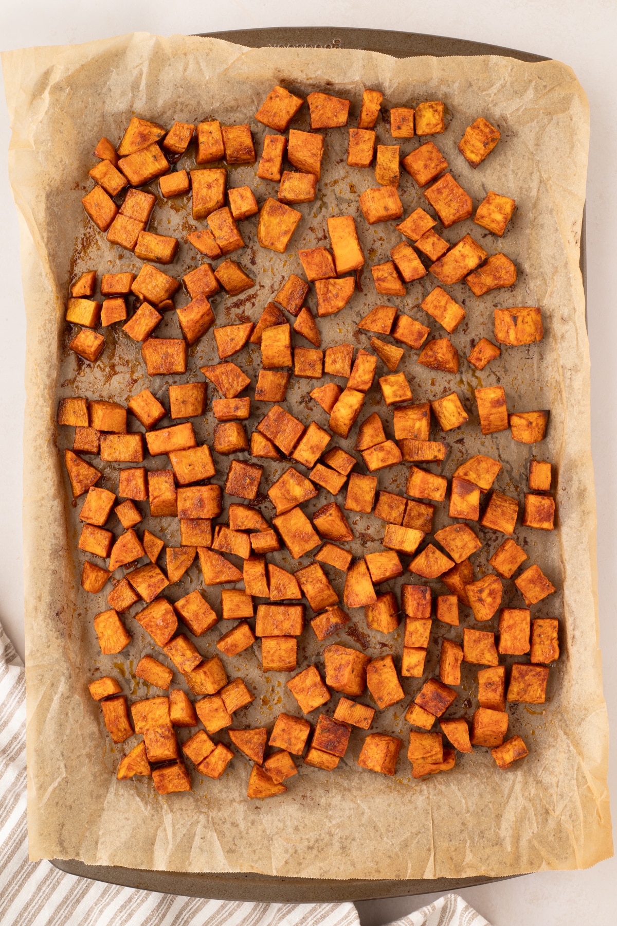 A sheet pan filled with roasted sweet potato cubes that have been seasoned. 