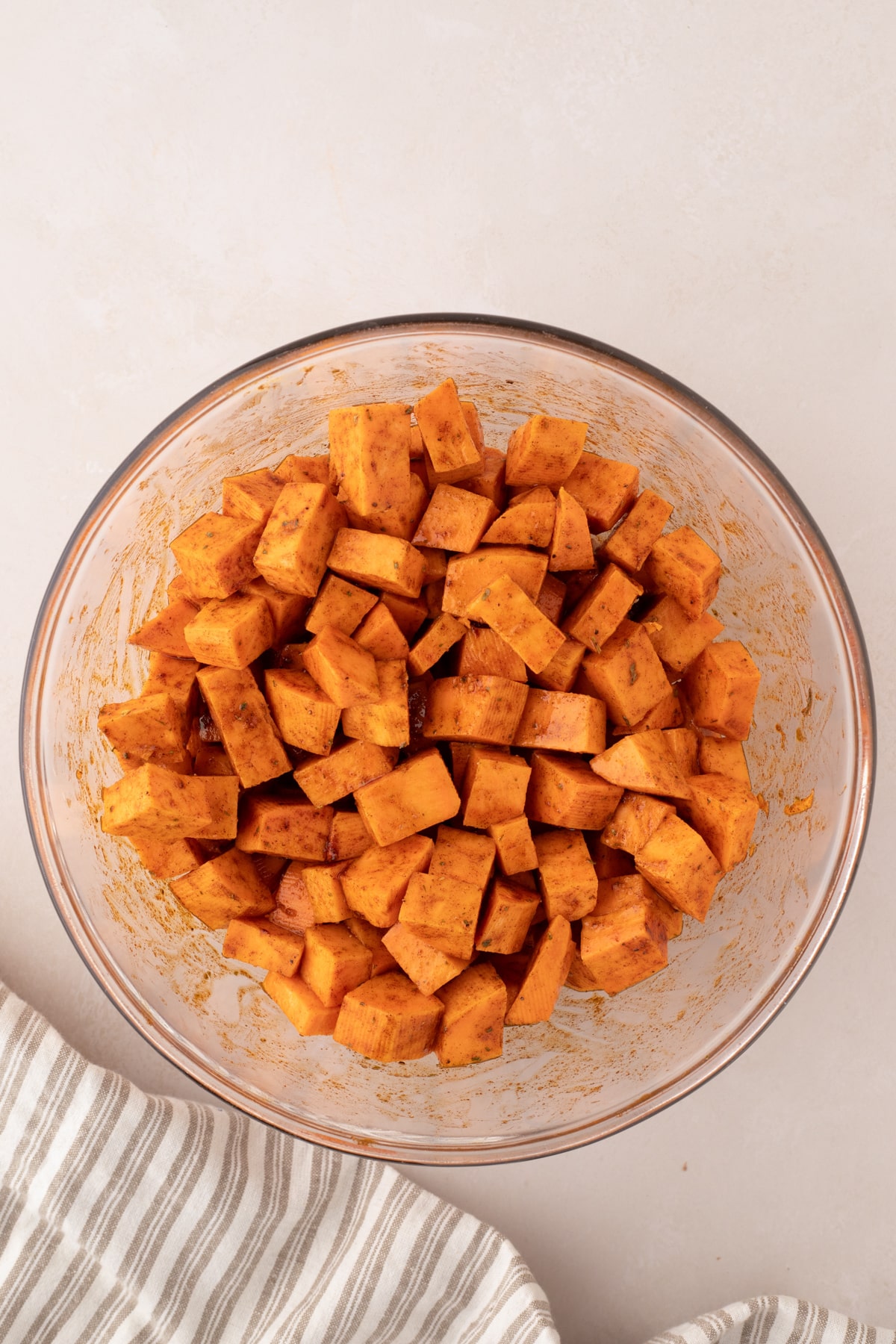 A bowl of cubed sweet potatoes tossed in seasonings and oil.