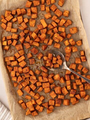 A sheet pan filled with roasted sweet potato cubes, with a spoon taking a portion.