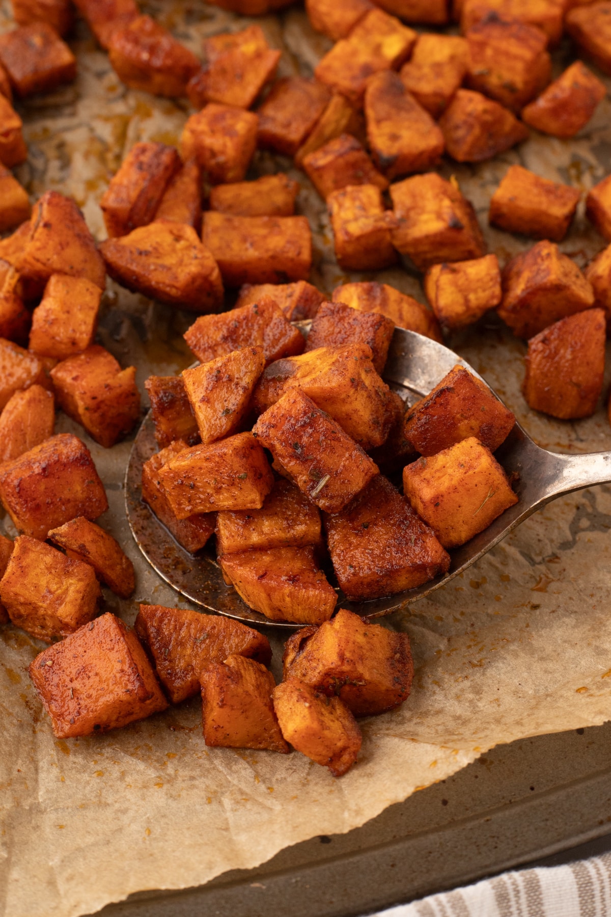 A spoon scooping up sweet potato cubes from a roasting pan.
