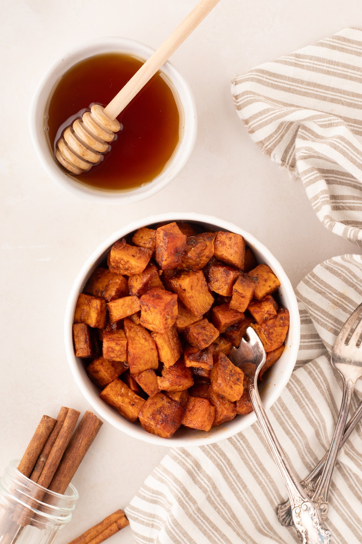 A bowl filled with roasted sweet potatoes, with a small bowl of honey on the side.