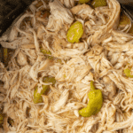 Shredded chicken stirred into juices in a slow cooker.