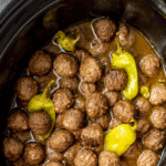 A slow cooker filled with meatballs and garnished with pepperoncini peppers.