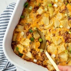 A spoon taking a portion of potato casserole from a baking dish.
