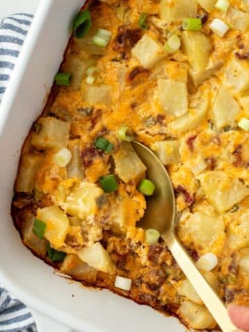 A spoon taking a portion of potato casserole from a baking dish.