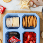A sectioned lunch container with meat, cheese, crackers, fruit, and a mini chocolate bar.