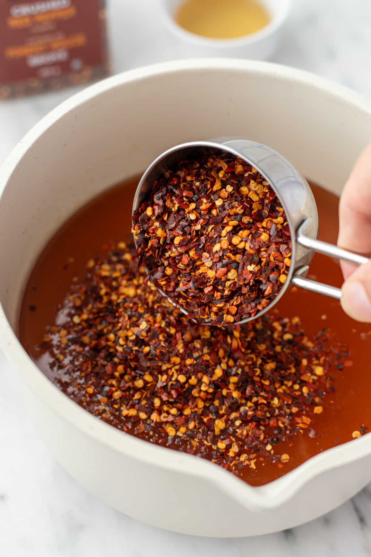 Adding dried red pepper flakes to a saucepan with honey.