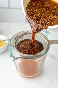 Pouring infused honey through a fine mesh strainer.