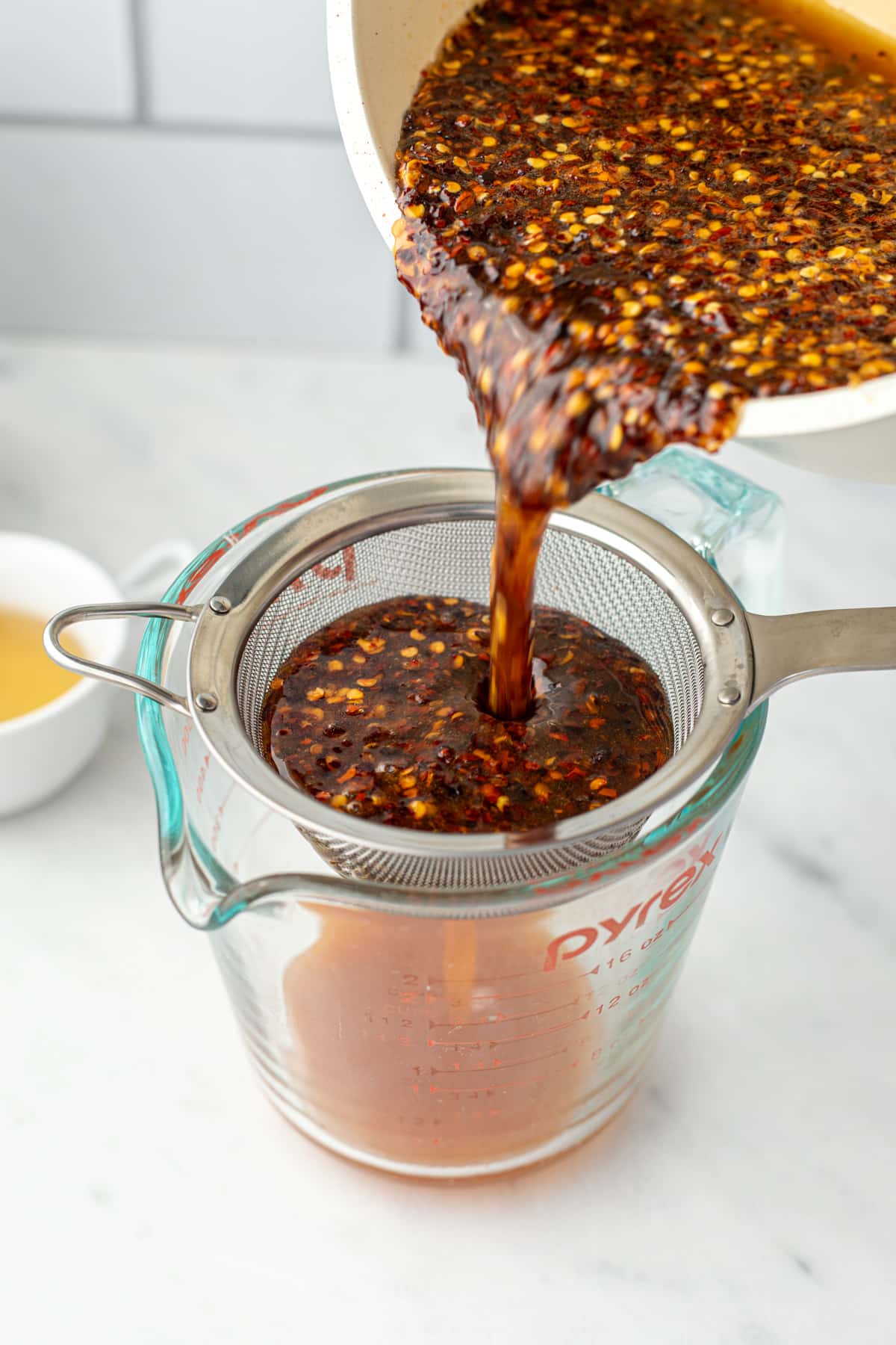 Pouring infused honey through a fine mesh strainer.