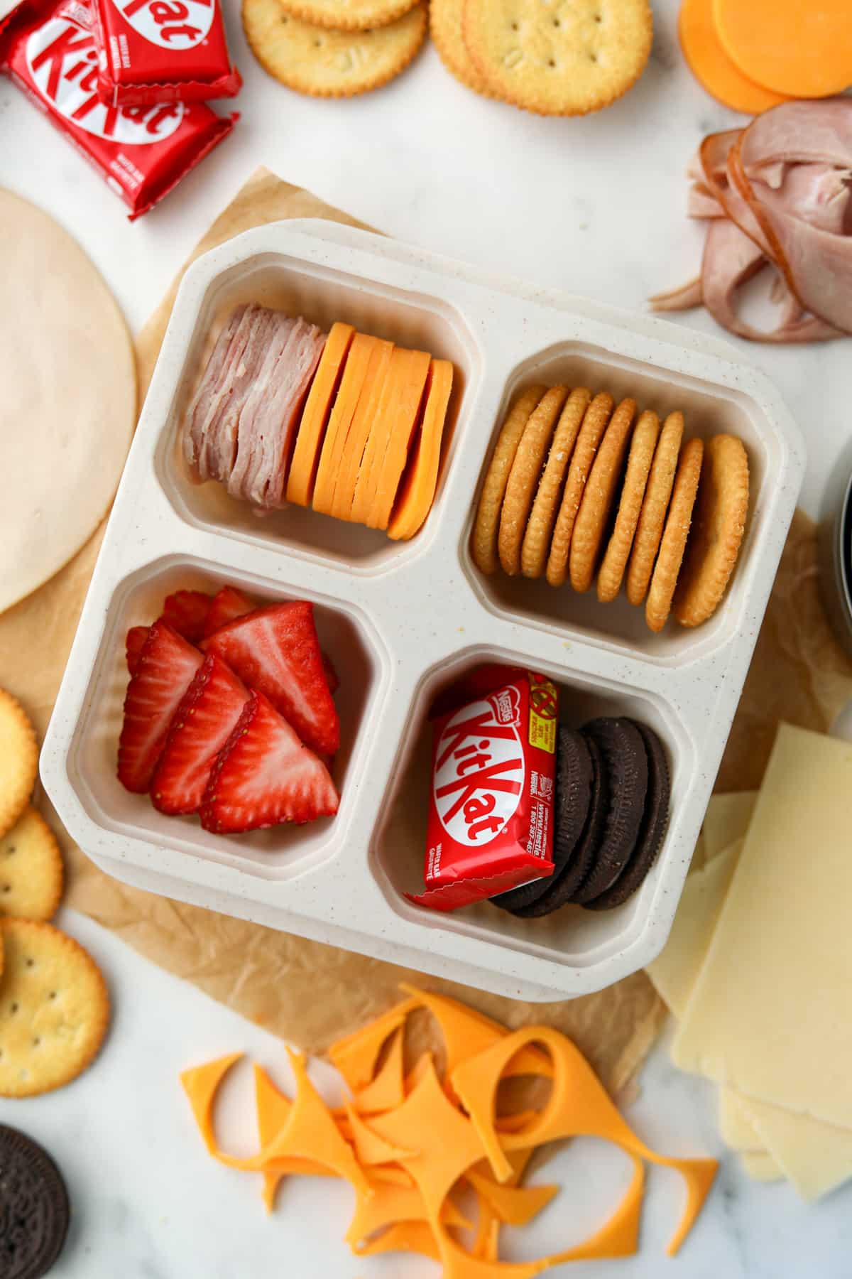A 4 compartment container with crackers, deli meat, cheese, and sweet treats.
