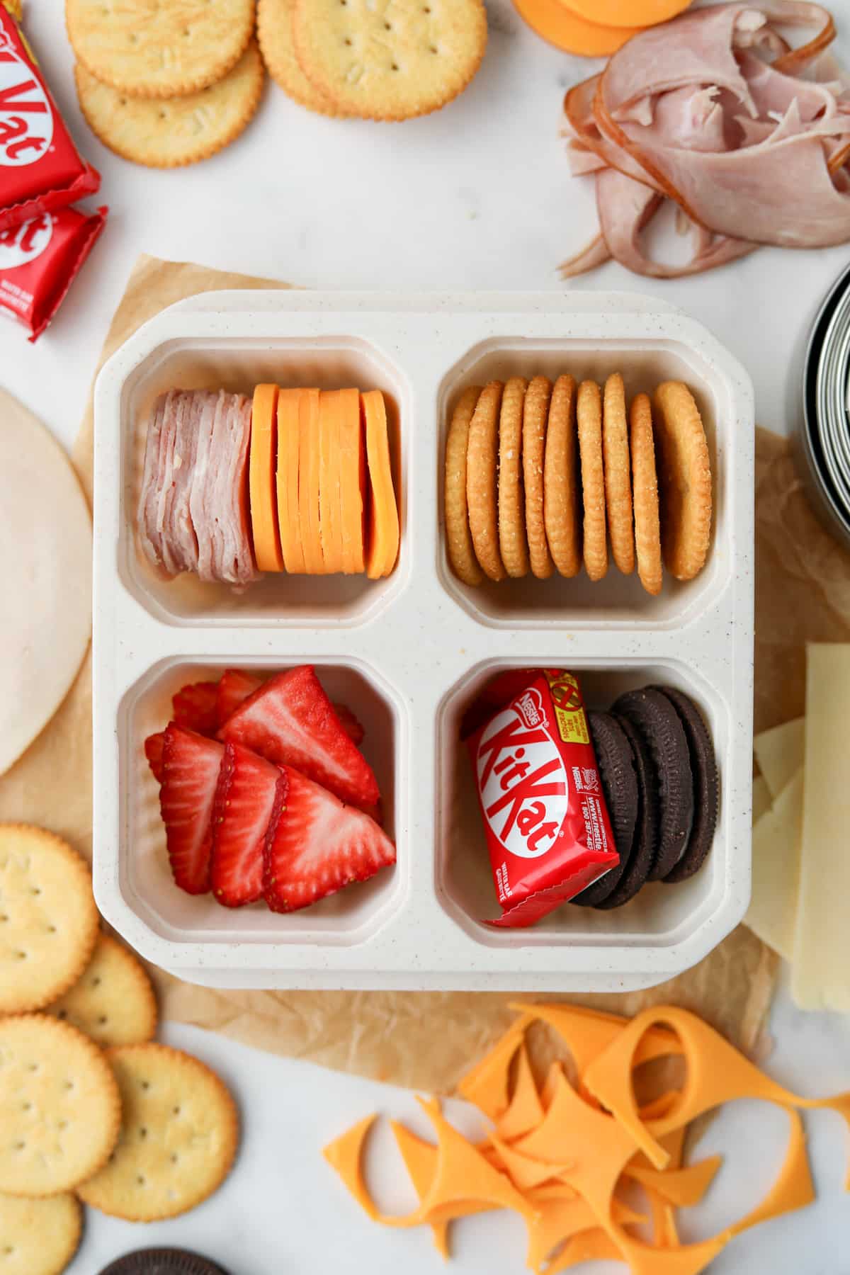 A lunch container filled with cheese, crackers, fruit, mini chocolate bar, and cookies.