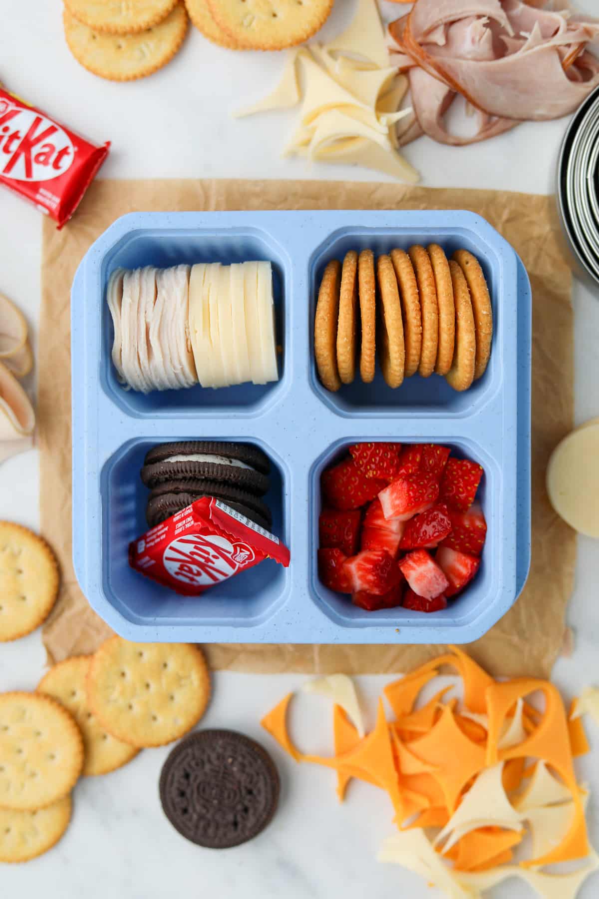 A lunch container filled with cheese, crackers, fruit, and a mini chocolate bar.