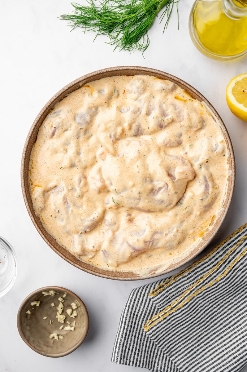 A bowl filled with yogurt marinade and chicken pieces.